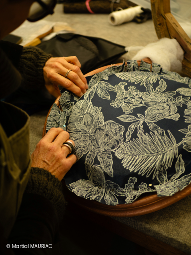 Geste technique d'un apprenant en atelier de garnissage traditionnel travaillant sur la pose de tissu pour la restauration d'une chaise.