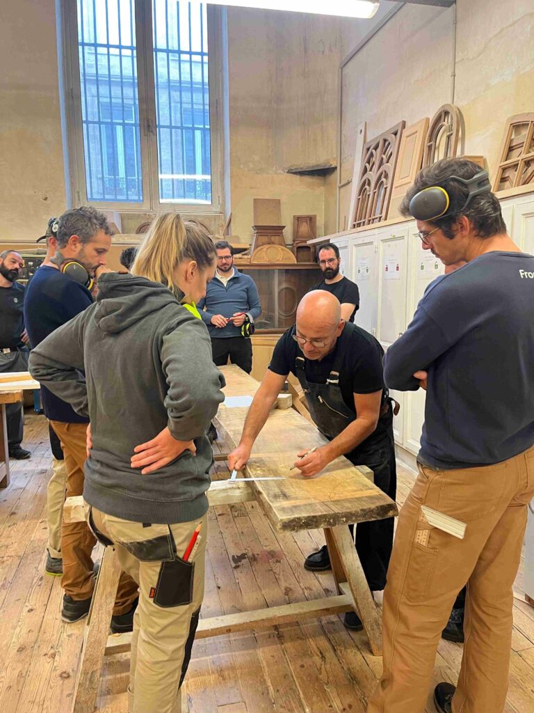 Un formateur de la Philomathique transmettant les techniques de menuiserie traditionnelle dans le cadre historique de l'école fondée en 1808 à Bordeaux.