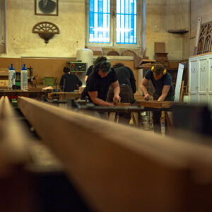 Deux apprenants dans l'atelier bois de la Philomathique de Bordeaux effectuent le ponçage manuel d'une pièce en bois dans l'atelier.