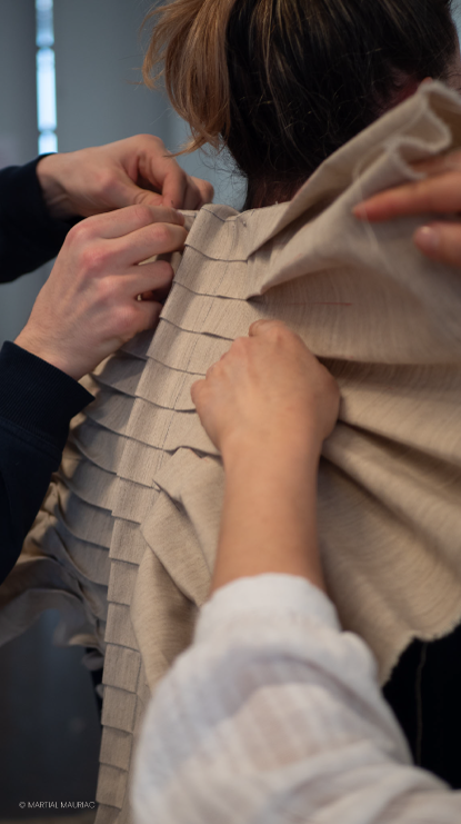 Gros plan sur les mains d'un apprenant du pôle mode de la Philomathique ajustant avec précision un vêtement pour le défilé Mesure et Démesure.
