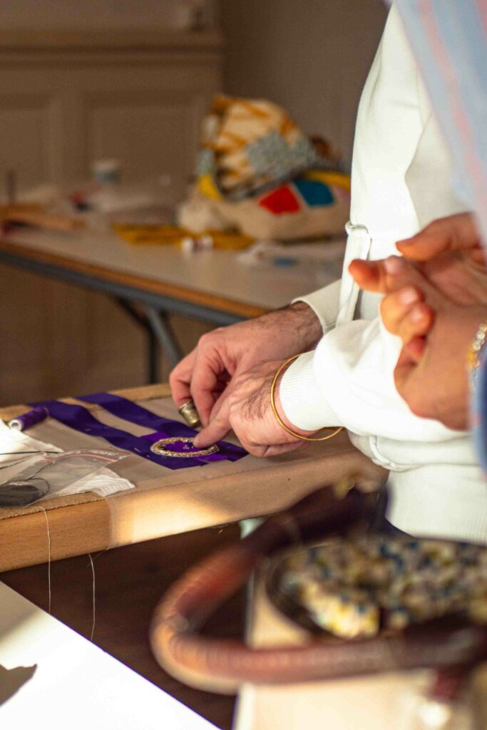 Un intervenant en broderie de la Philomathique de Bordeaux guidant un élève lors d'un atelier de découverte de l'art de l'aiguille.